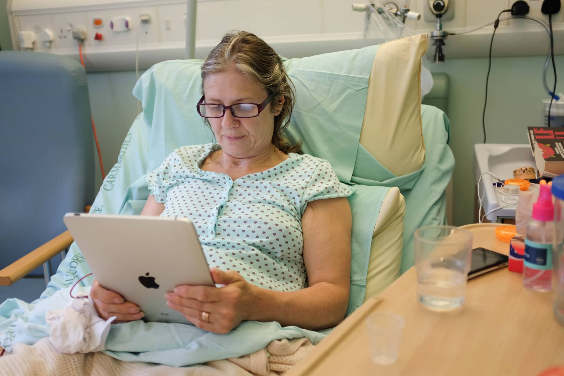A Middle Aged Woman Reading Her Ipad, Recovering In A Nhs Hospital Bed After A Hip Replacement Operation Uk